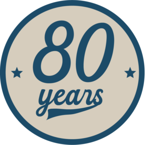 80th anniversary emblem: round beige badge with dark blue border and stars surrounding the text 80 years
