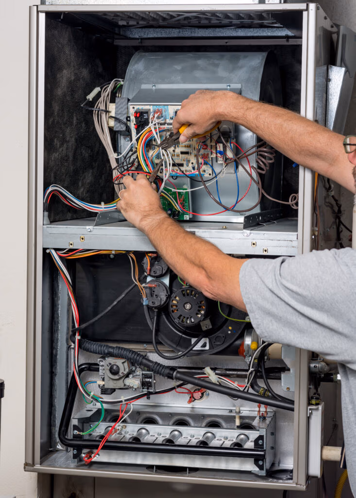 Technician servicing a furnace control board inside an open HVAC cabinet, wiring and components visible