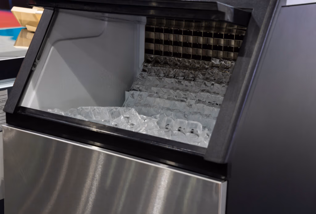 Open stainless steel ice maker drawer showing stacked ice cubes and metal rack inside.