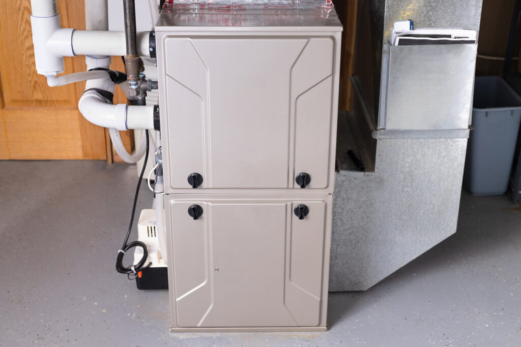 Residential furnace in a basement with white PVC venting pipes and a large metal HVAC duct nearby